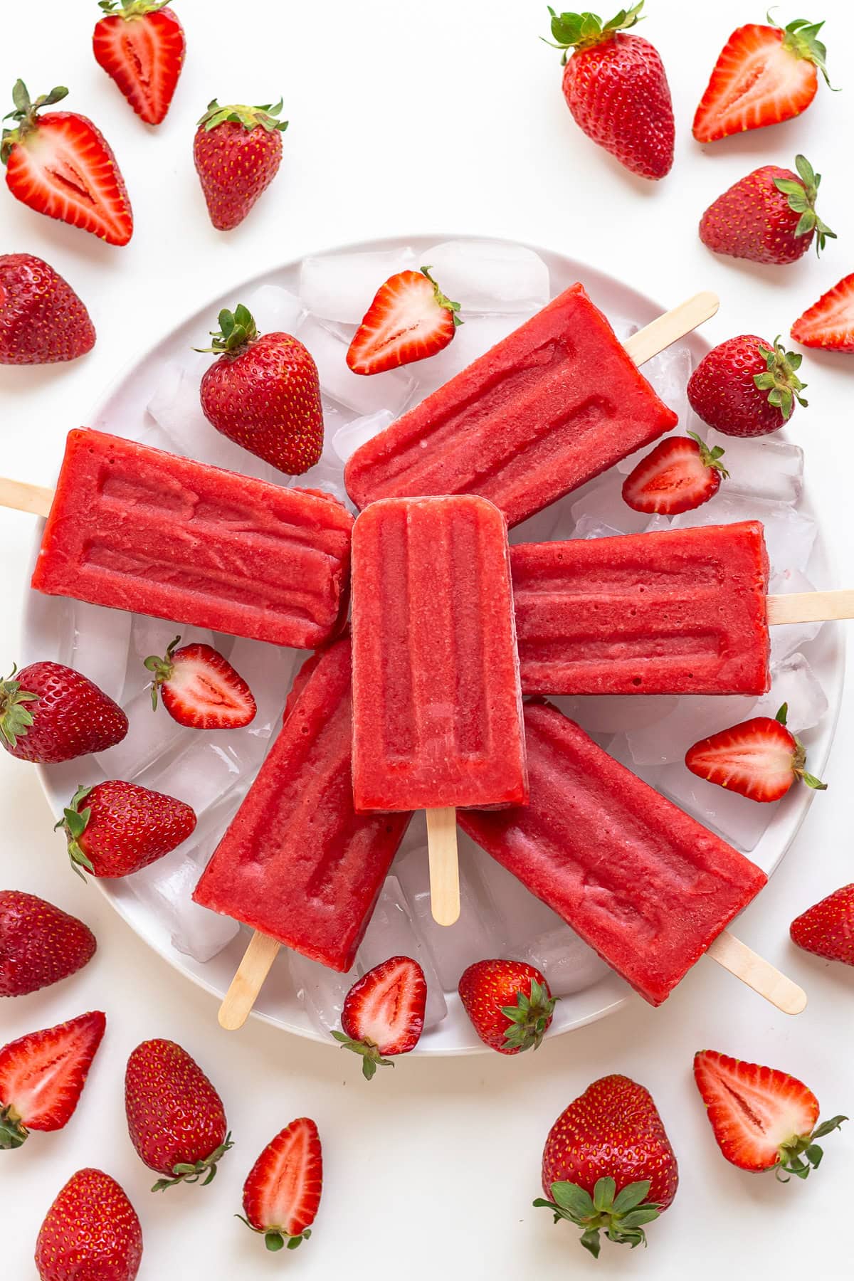 Strawberry popsicles on a plate of ice surrounded by fresh strawberries.