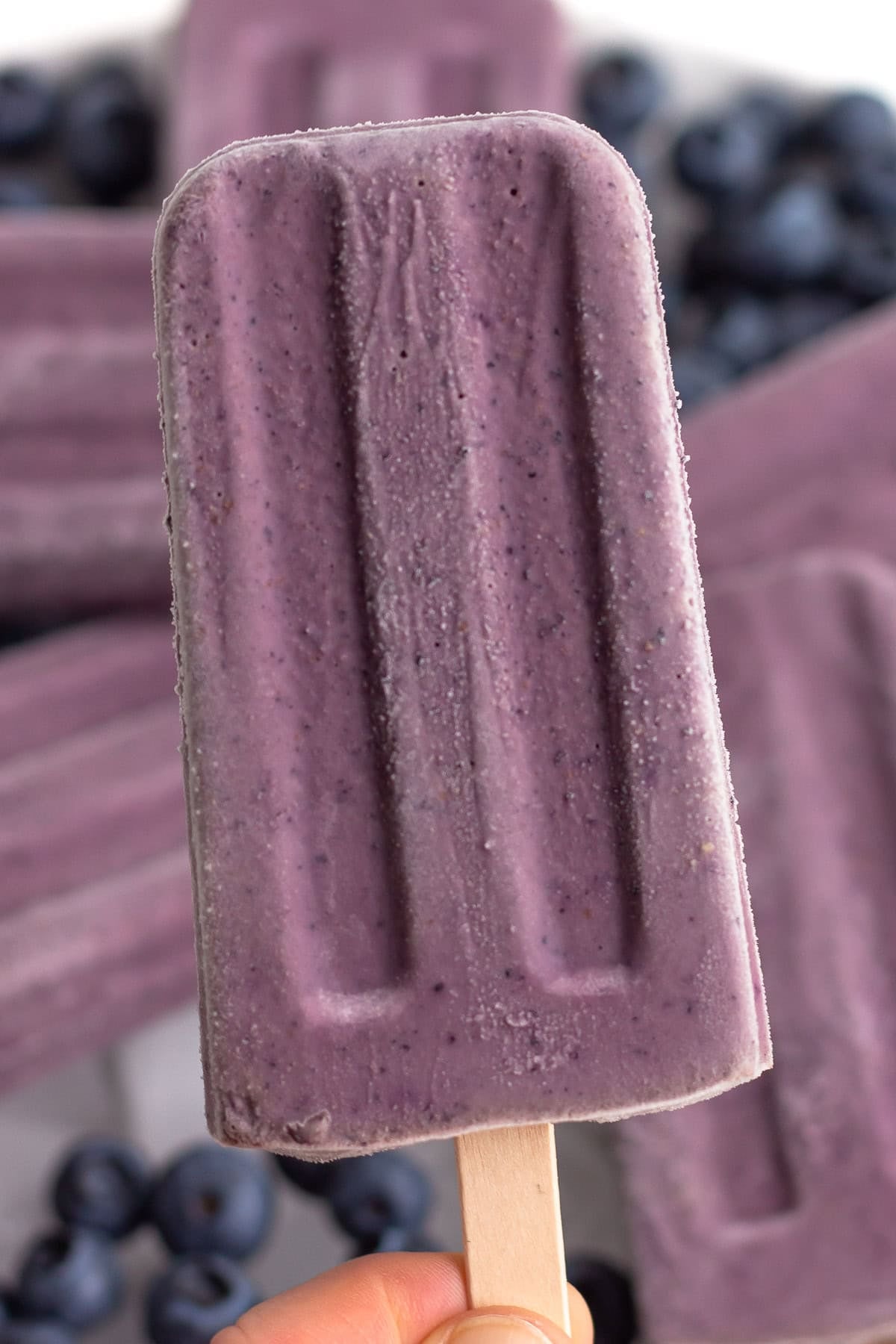 Hand holding a blueberry yogurt popsicle.
