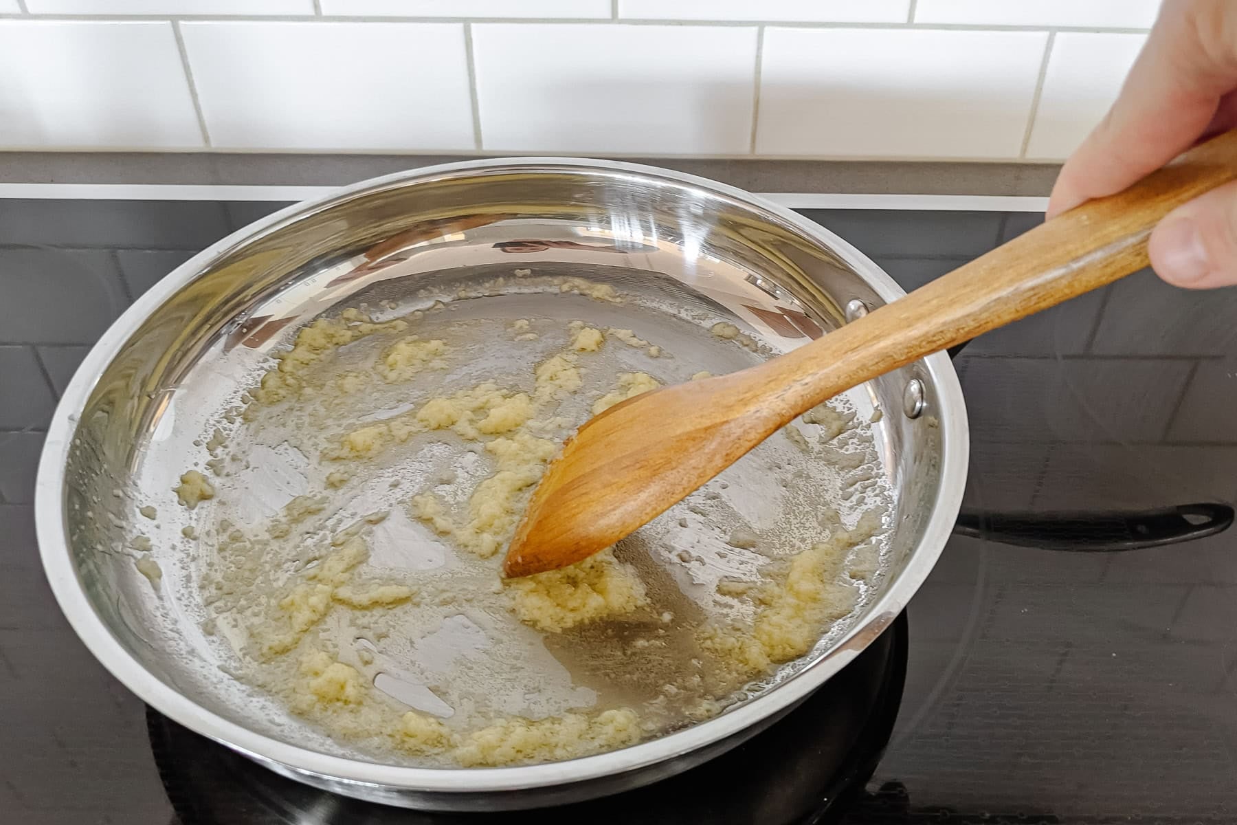 Garlic being sauteed in butter in a stainless steel pan.