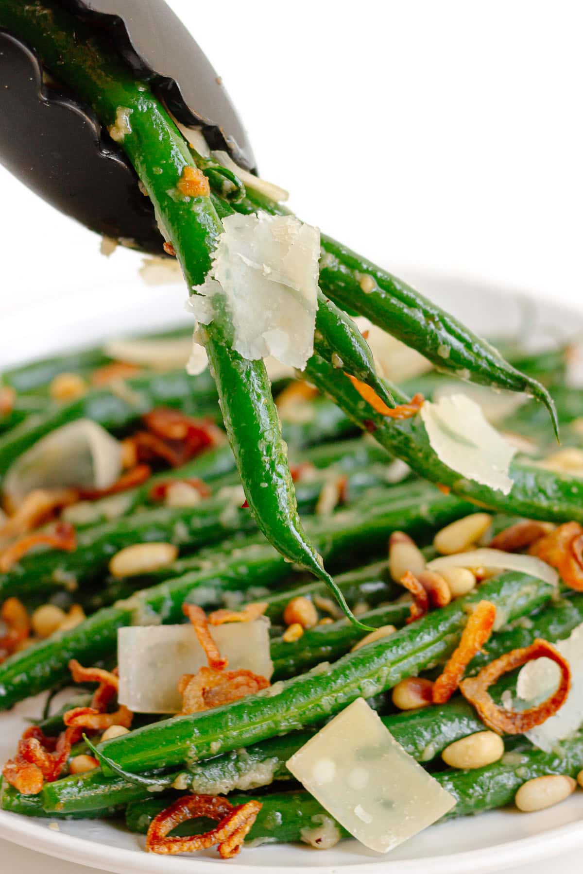 Tongs picking up some garlic butter green beans from serving plate.